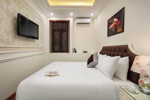 A neatly made bed with a book, a television mounted on the wall, and a window with blinds. - Bastra Classy Hotel (Hoan Kiem Ward)
