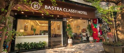 Ein Hotel Eingang mit einem Schild mit der Aufschrift 'BASTRA CLASSY HOTEL', einem Empfangstresen und Zimmerpflanzen.