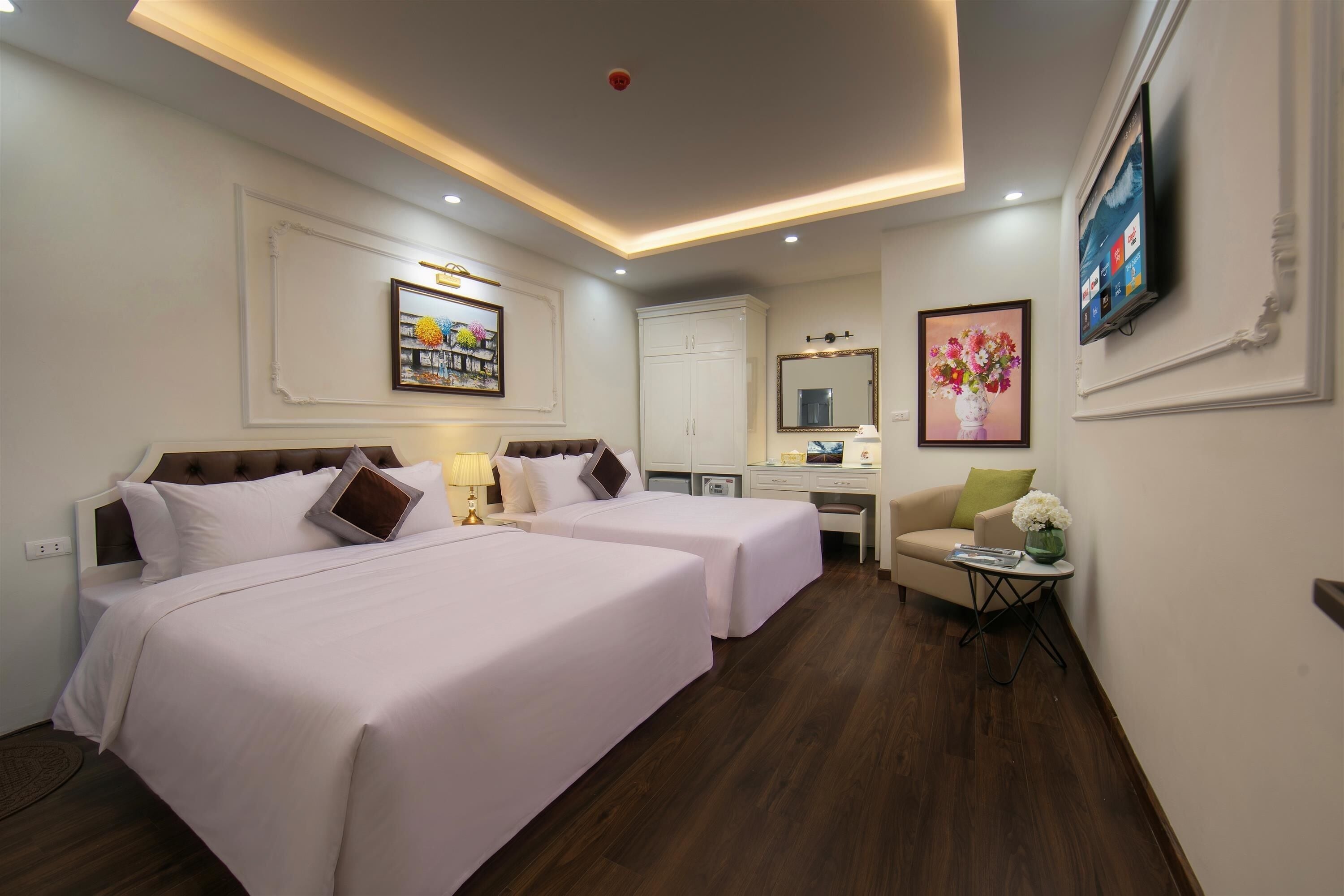 A hotel room with two beds, a desk, a chair, a TV, and artwork on the walls.