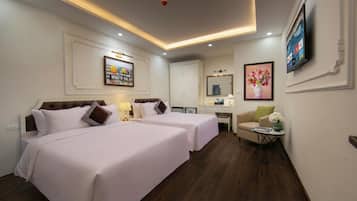 Habitación de hotel con dos camas, un escritorio, una silla, un televisor y obras de arte en las paredes.
