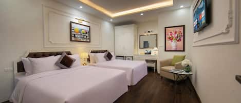 A hotel room with two beds, a desk, a chair, a TV, and artwork on the walls.