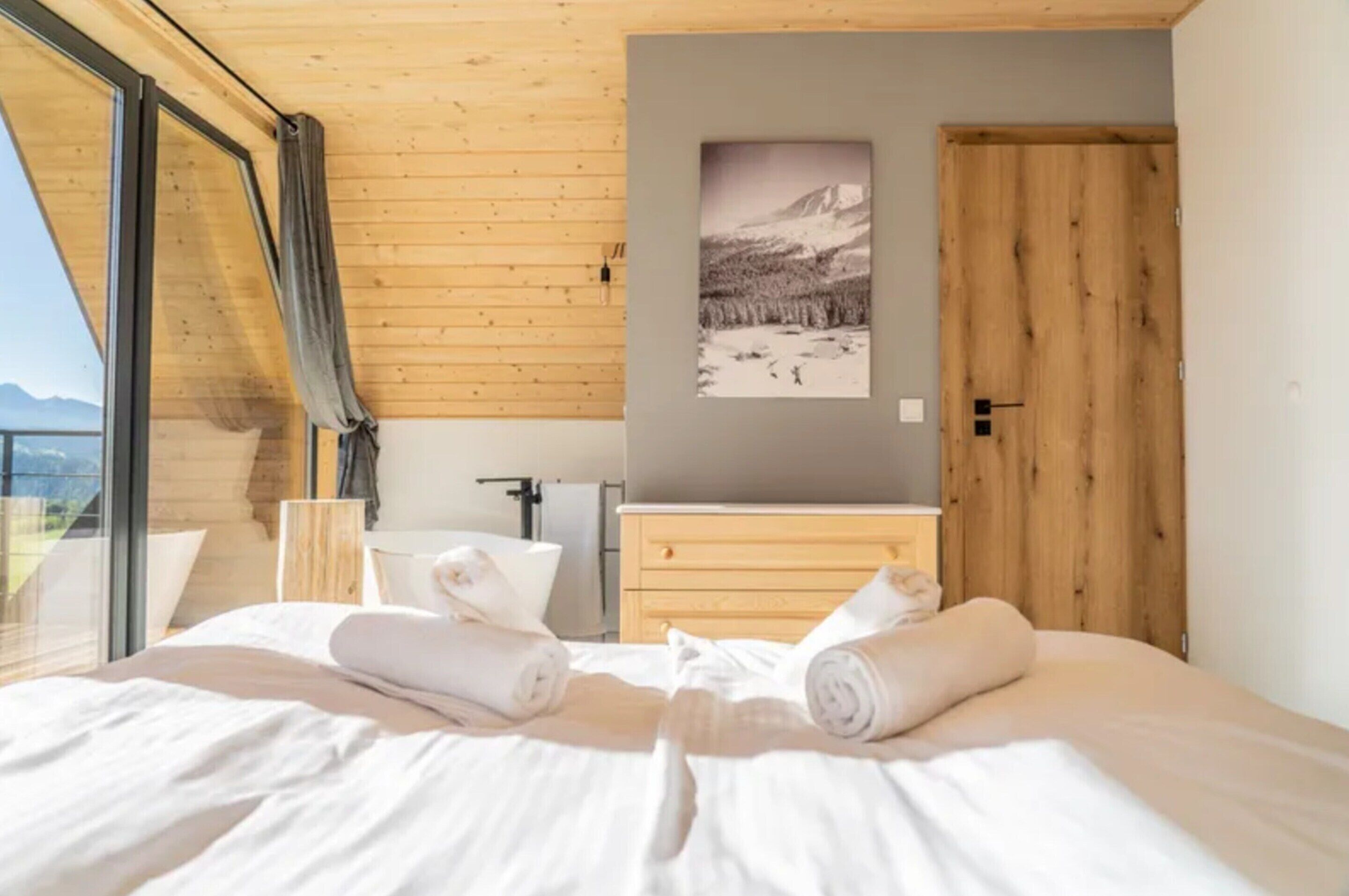 A bedroom with a bed, towels, a wooden dresser, a painting, and a door.