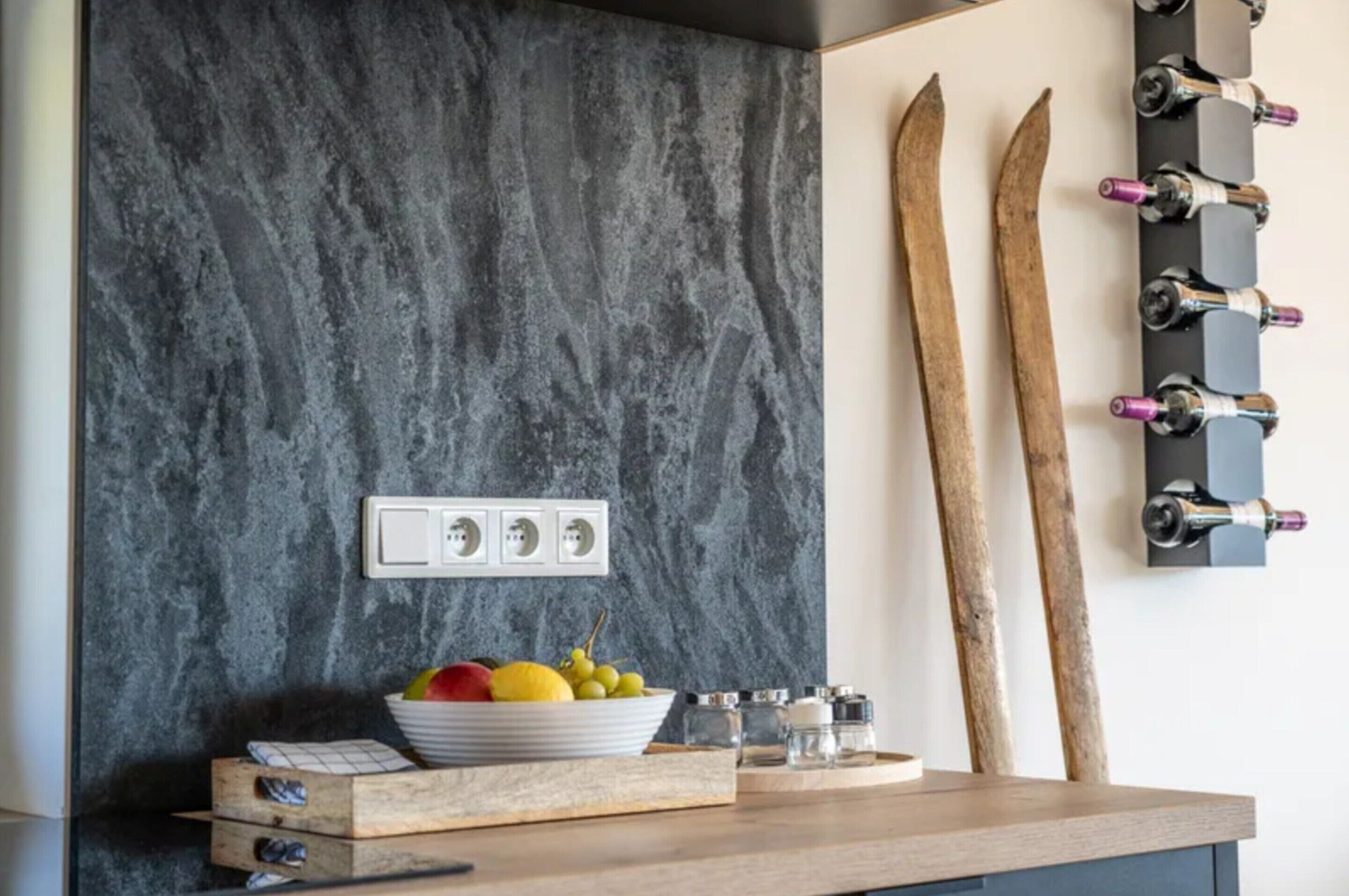 Una cocina con salpicadero de mármol, un frutero, saleros y pimenteros, y esquíes de madera en la pared.