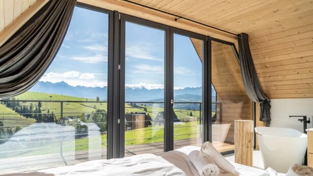Ein Schlafzimmer mit großem Fenster, einem Bett, einer Holzbalkendecke und einer weißen Badewanne.