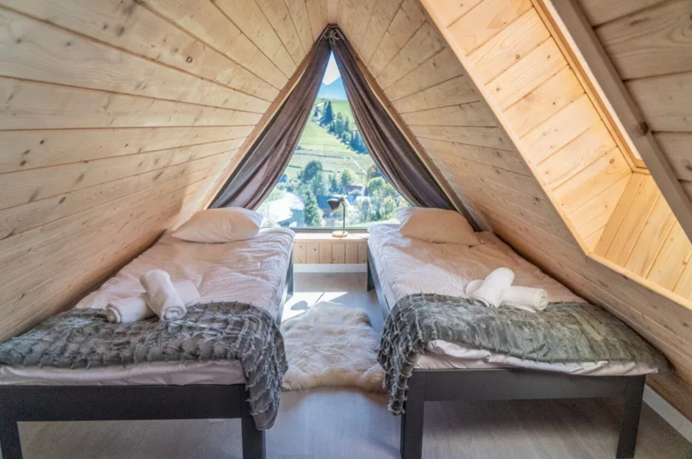 A room with two beds, a wooden ceiling, and a view of the landscape.