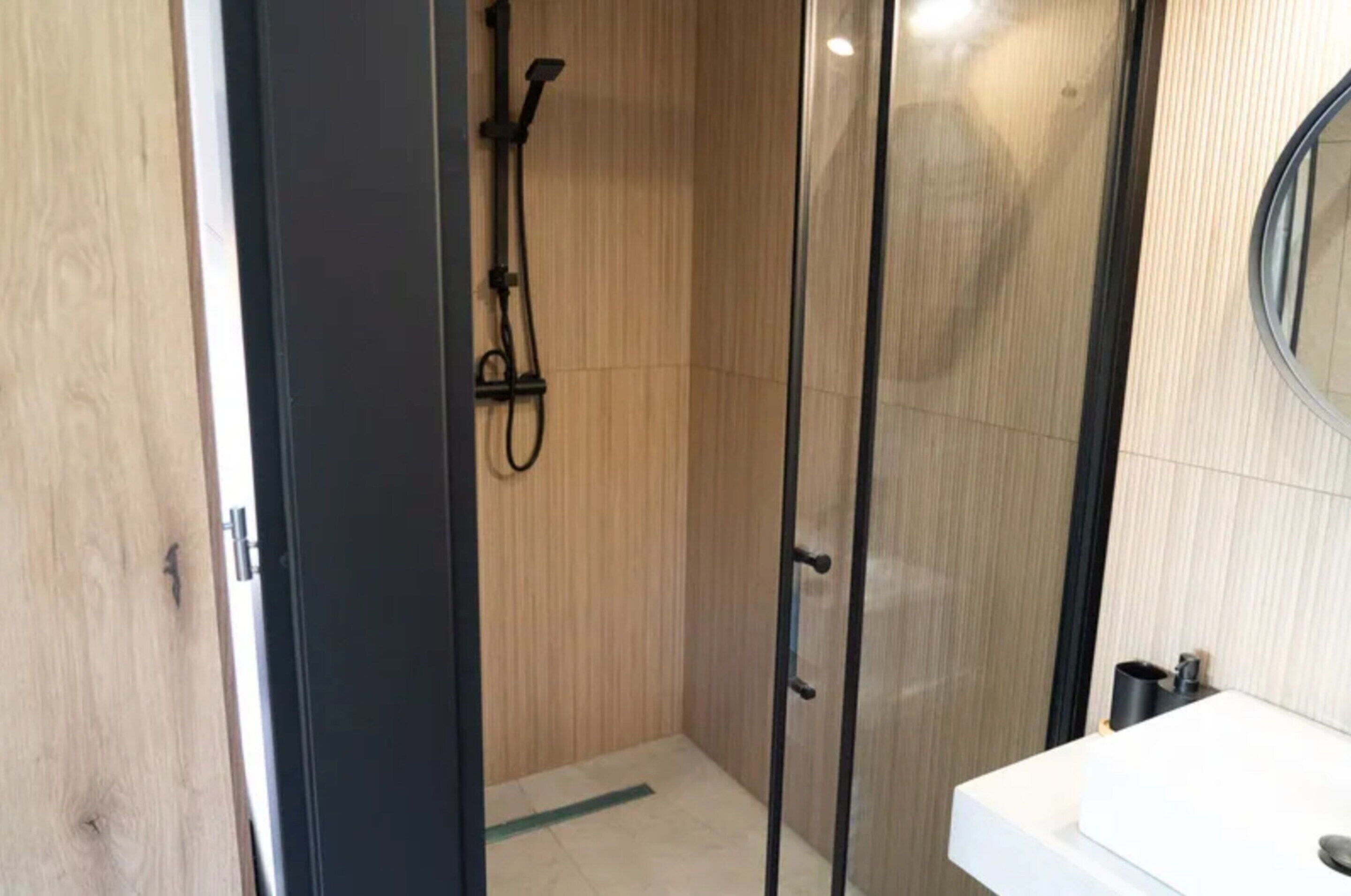 A modern bathroom with a glass shower enclosure, a white sink, and a wooden wall.