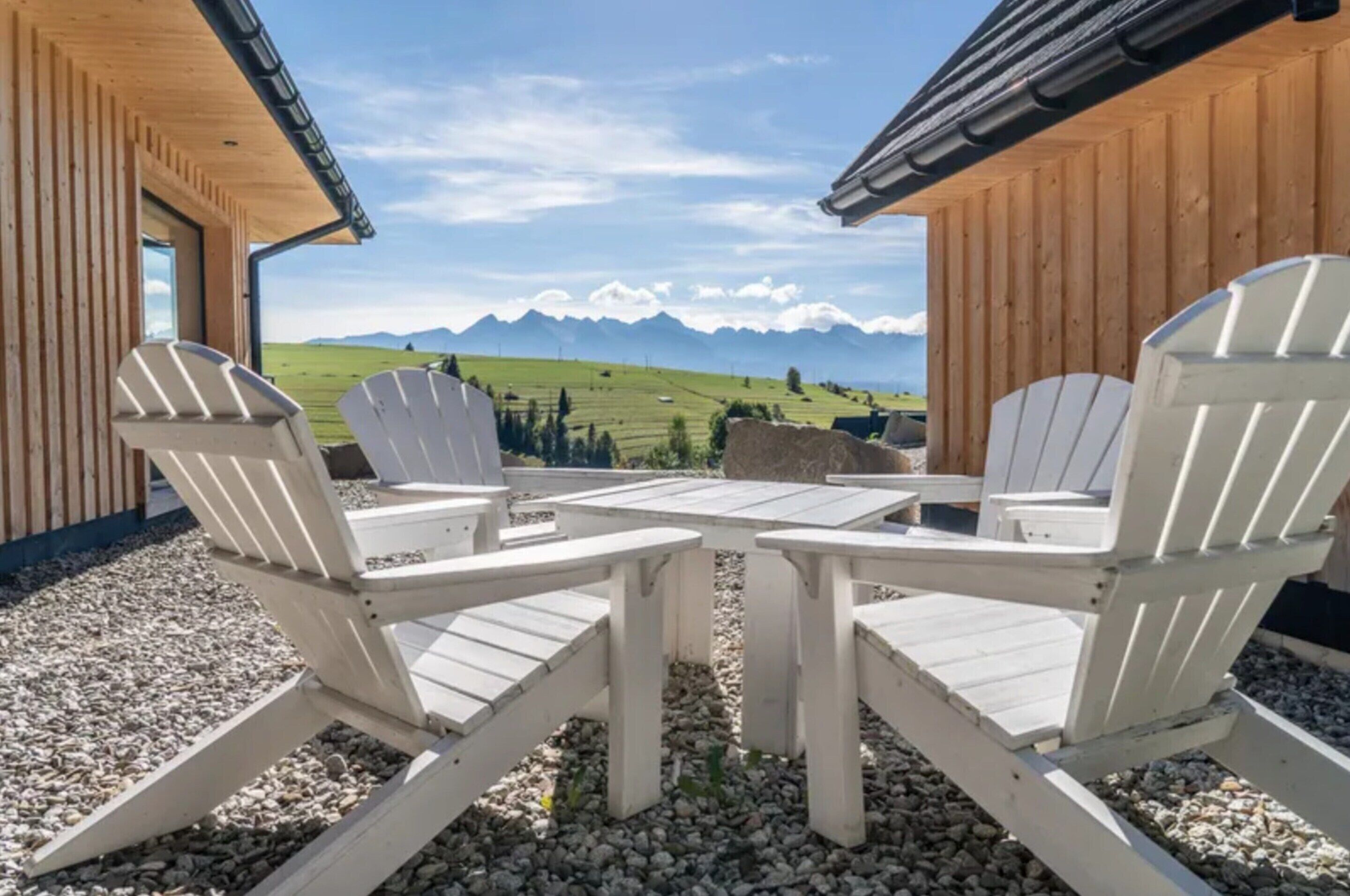 A wooden building with a view of mountains. There are Adirondack chairs and a table outside.