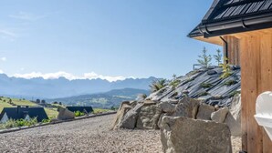 Ein Holzhaus mit geneigtem Dach, einer Schotterauffahrt und Blick auf ferne Berge.