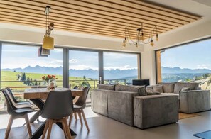 A modern living room with a large sofa, dining table, and chairs, large windows with a mountain view. - Home With a Bathtub Overlooking the Mountains (Bukowina Tatrzanska)