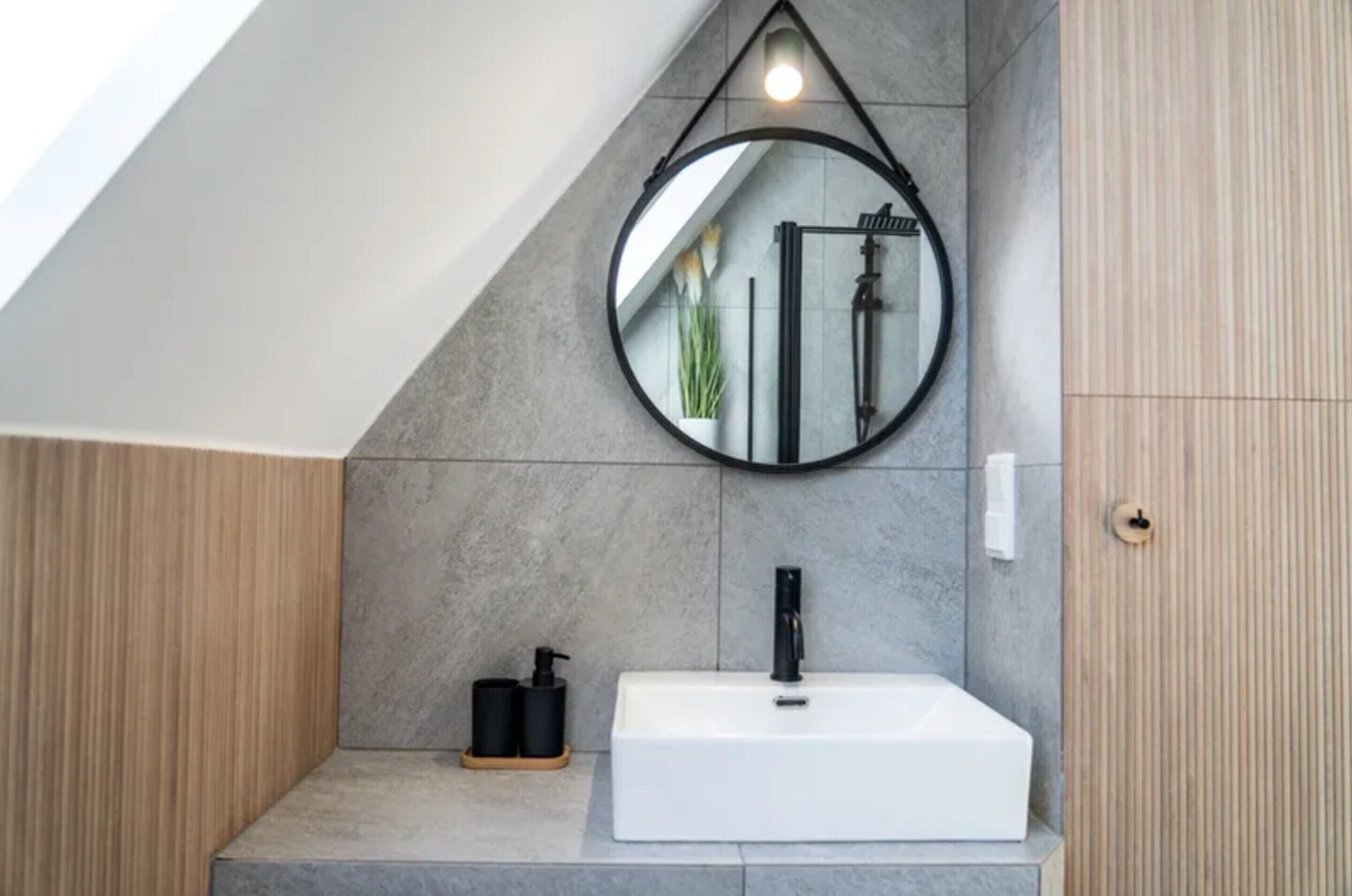 A modern bathroom with a white sink, a round mirror, and a towel rack.
