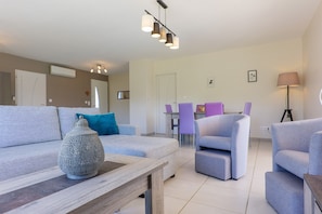 A modern living room with a sofa, armchairs, a coffee table, and a dining area with chairs.