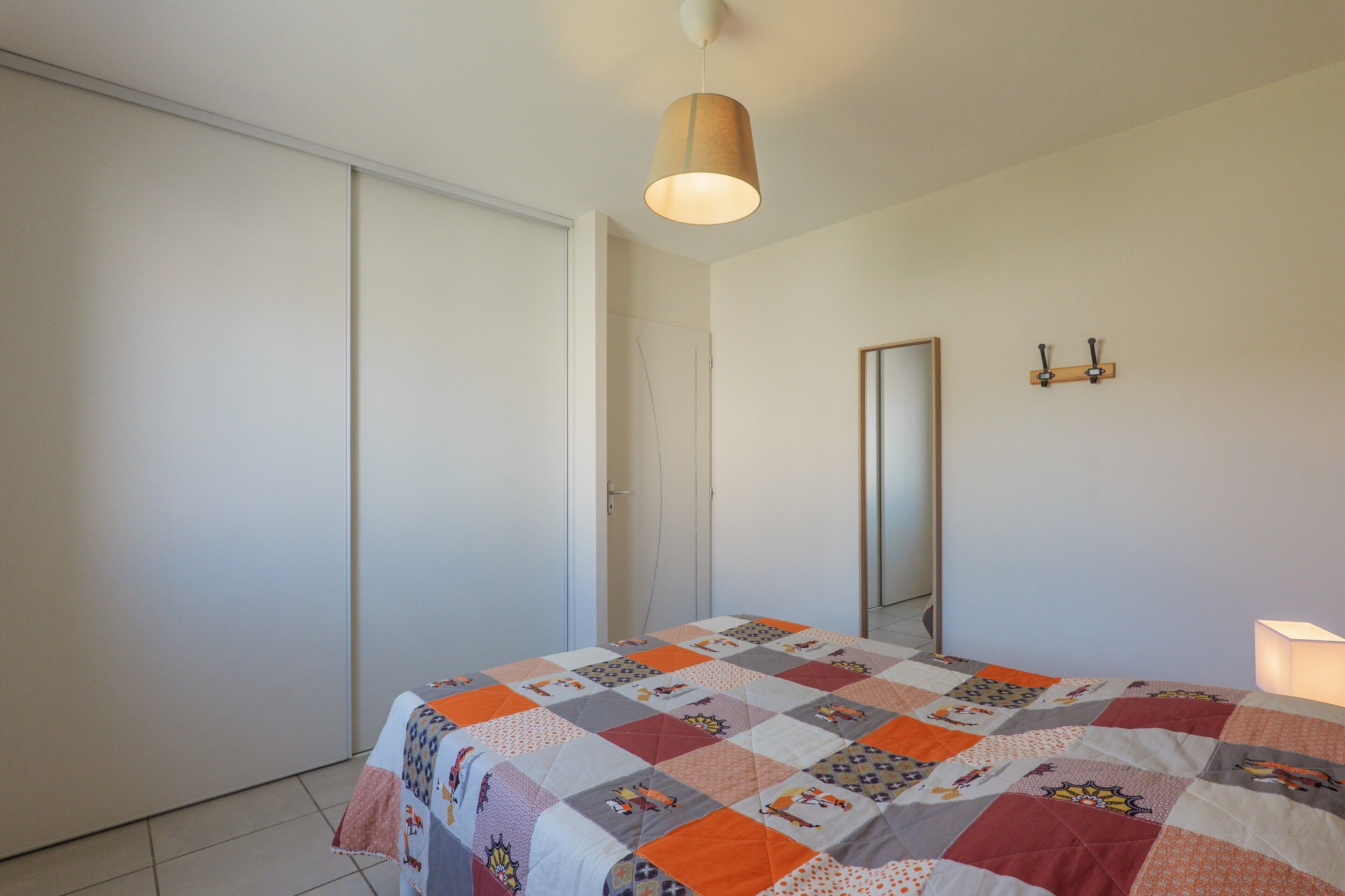 Ein Schlafzimmer mit Bett, einer Hängelampe, einem Spiegel und einer Tür.