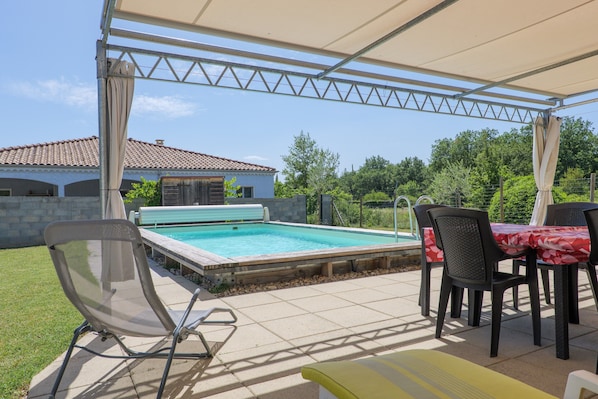 A covered outdoor area with a pool, chairs, and a table.