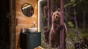 A bathroom with a wooden wall, a round mirror, a sink, and a bear mural. - Glamp Mała Łąka Jacuzzi & Sauna Zakopane (Zakopane)