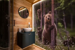 Een badkamer met een houten wand, een ronde spiegel, een wastafel en een muurschildering van een beer.