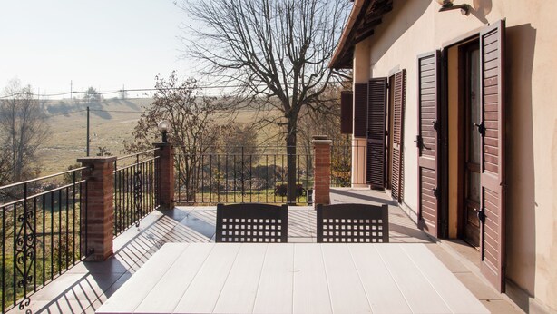 Een balkon met uitzicht op een landelijk landschap, een bakstenen pilaar en een deur met luiken.