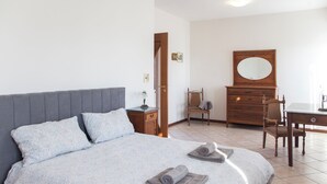 Een slaapkamer met een bed, een houten dressoir, een stoel en een bureau.
