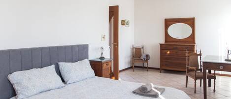 Un dormitorio con una cama, un aparador de madera, una silla y un escritorio.