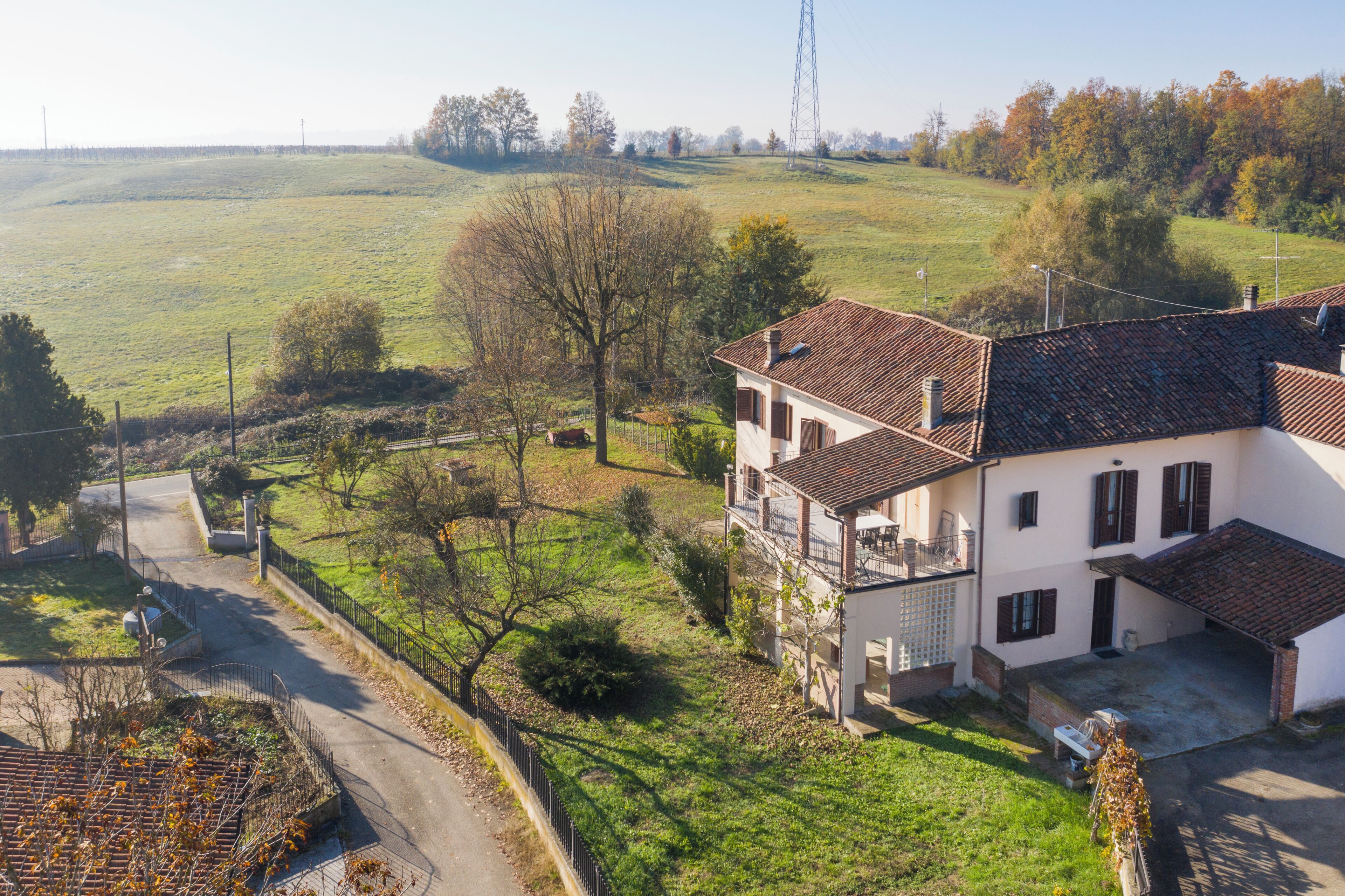 Une maison à deux étages avec un balcon, une allée pavée et un champ verdoyant en arrière-plan.