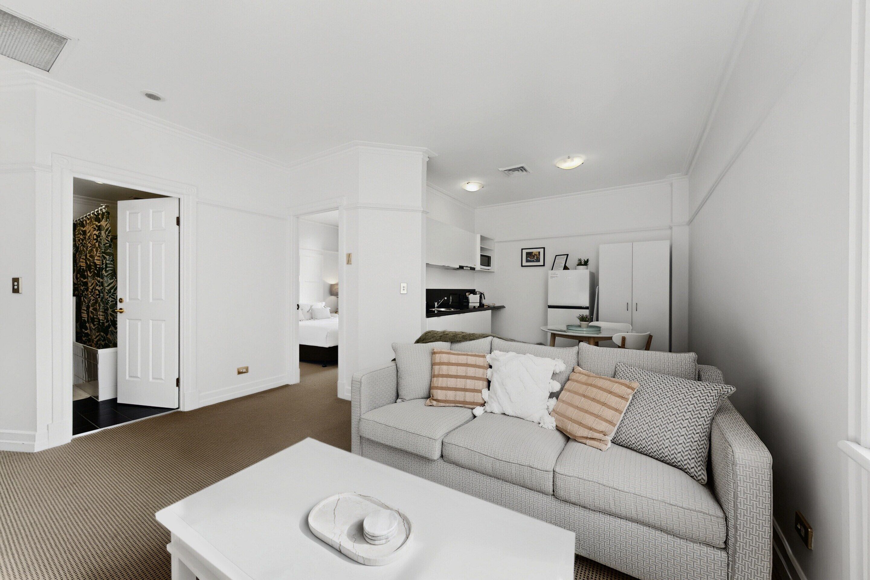 A modern living room with a grey sofa, a white coffee table, and a kitchen area in the background.