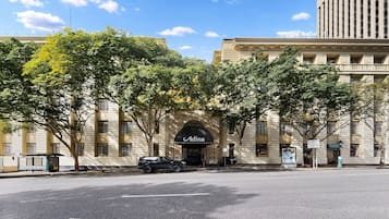 A building with a large arched entrance labeled 'Adina,' a paved street, and a parked car.