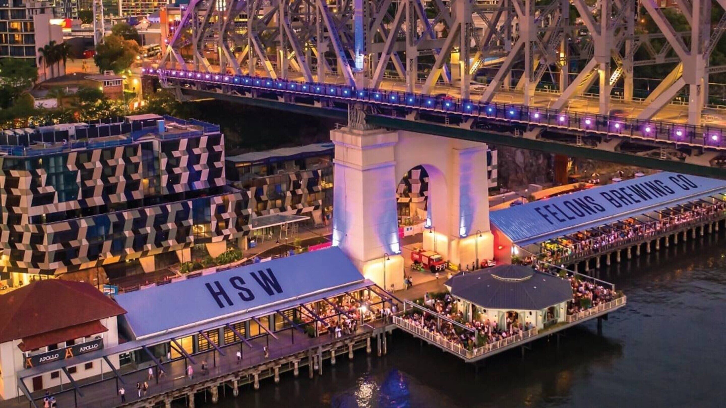 A waterfront restaurant with a view of a bridge, a sign for 'FELLOWS BREWING CO.', and a sign for 'HSW'.