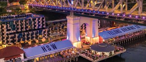 A waterfront restaurant with a view of a bridge, a sign for 'FELLOWS BREWING CO.', and a sign for 'HSW'.