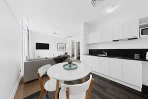 A modern kitchen with white cabinets, a black countertop, and a dining area with a white table and chairs. - Skyline 1-bed Retreat in Brisbane City (Brisbane)