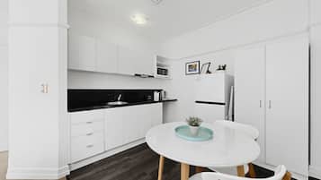 A modern kitchen with white cabinetry, a black countertop, a white dining table with chairs, and a small potted plant on the table.