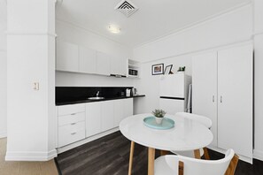 A modern kitchen with white cabinetry, a black countertop, a white dining table with chairs, and a small potted plant on the table. - Skyline 1-bed Retreat in Brisbane City (Brisbane)
