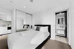 A modern hotel room with a large bed, a bedside table, a wardrobe, and a bathroom with a mirror and sink. - Elevated 2-bed Stay Steps From Crown (Melbourne)