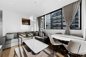 A modern living room with a sectional sofa, a coffee table, and a dining area with chairs and a table. - Elevated 2-bed Stay Steps From Crown (Melbourne)