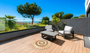 A balcony with a wooden floor, two white chairs, a small table, and a woven rug.