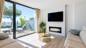 Uma sala de estar moderna com um sofá, uma mesa de centro, uma TV fixada na parede e uma lareira.