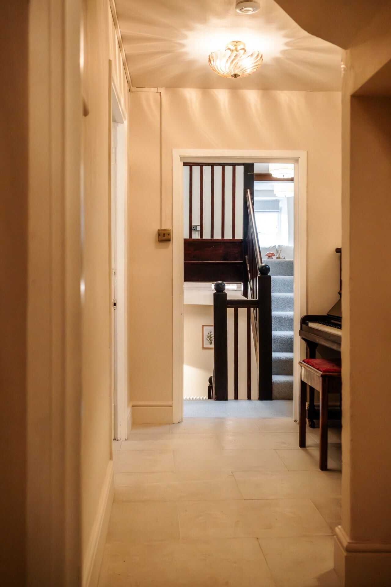 Een gang met een piano, een trap en een deur naar een andere kamer.