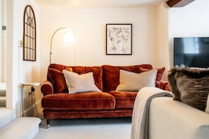 A living room with a red velvet sofa, a standing floor lamp, a framed botanical illustration, and a television. - A stylish, character-filled Cotswolds retreat in the heart of Chipping Norton, perfect for families and friends looking to reconnect. ✨ (Oxfordshire)