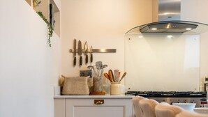 Cozinha moderna com armários brancos, coifa de aço inoxidável e um espaço de jantar com uma cadeira.