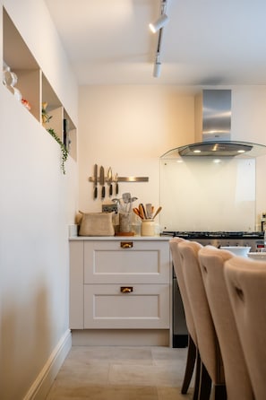 A modern kitchen with white cabinetry, a stainless steel range hood, and a dining area with a chair. - A stylish, character-filled Cotswolds retreat in the heart of Chipping Norton, perfect for families and friends looking to reconnect. ✨ (Oxfordshire)