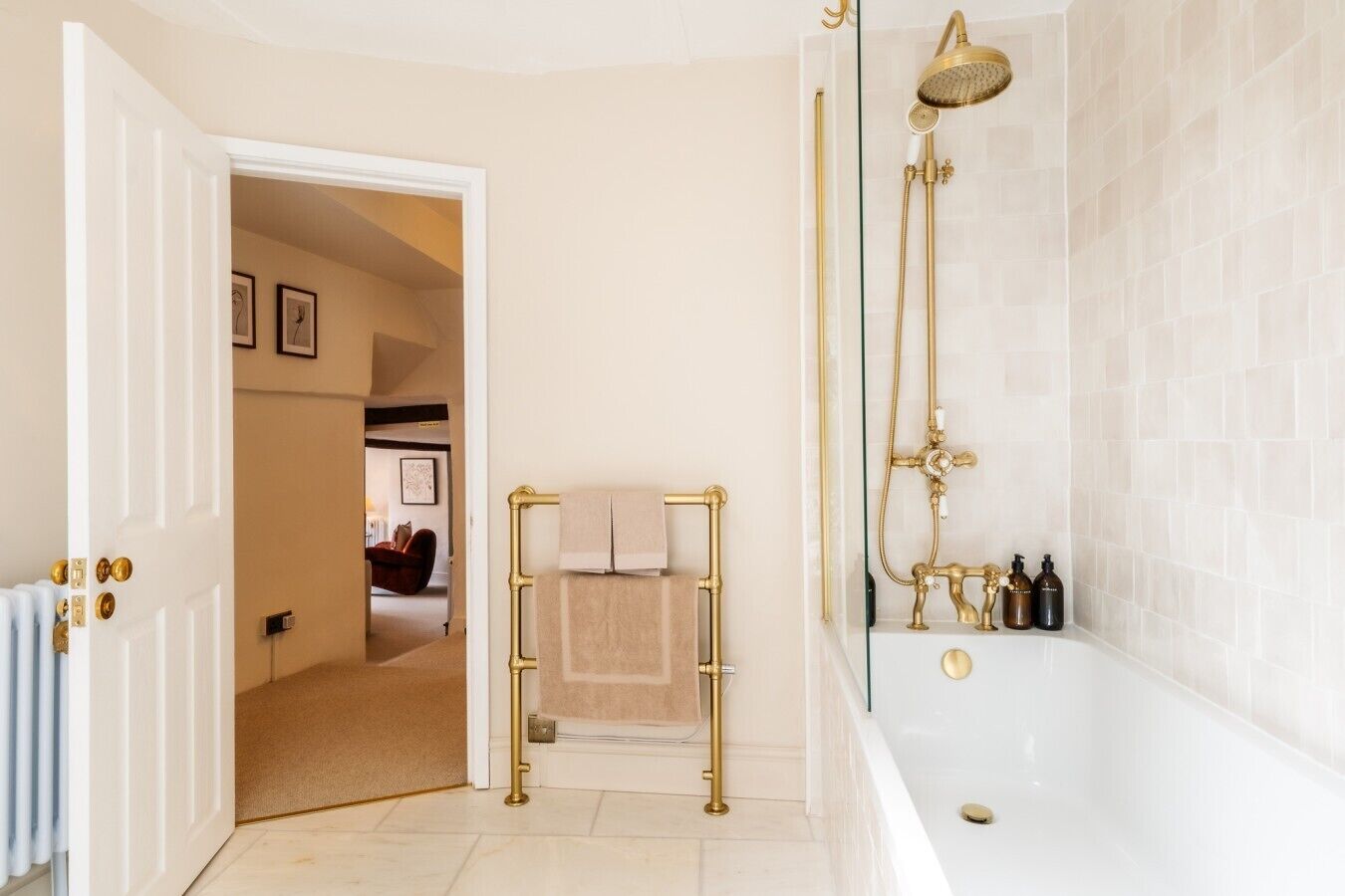 A bathroom with a white bathtub, gold fixtures, and a towel rack.