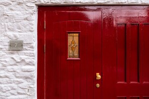 A red door with a brass knocker and a glass panel with a decorative design. A sign above the door reads 'MAISONETTE 7 HORSE FAIR.' - A stylish, character-filled Cotswolds retreat in the heart of Chipping Norton, perfect for families and friends looking to reconnect. ✨ (Oxfordshire)