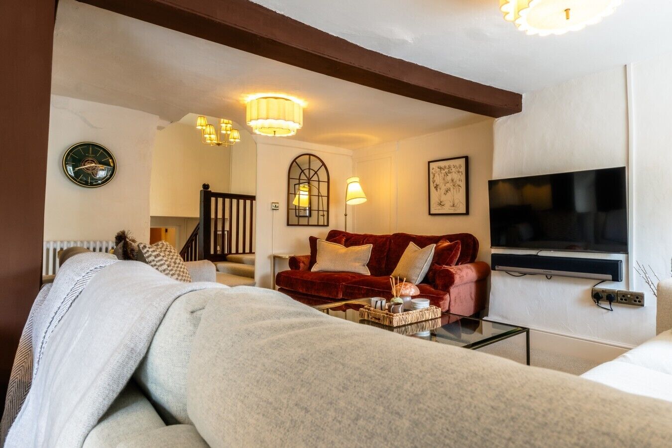 A living room with a sofa, a red velvet couch, a coffee table, a TV, and a staircase.