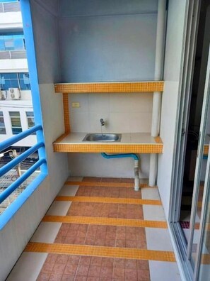 A small balcony with a sink, tiled floor, and a view of a building. - Bella B Plus Hotel (Bangkok)