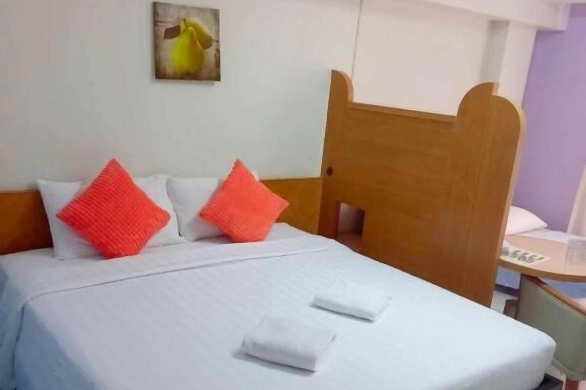 A bed with white bedding, two red pillows, and a wooden headboard.