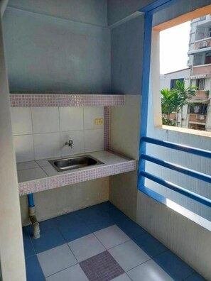 A small kitchen with a sink, tiled backsplash, and a window with a view of buildings. - Bella B Plus Hotel (Bangkok)