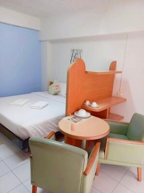 A hotel room with a bed, a small table with a chair, a wooden headboard, and a wall-mounted shelf. - Bella B Plus Hotel (Bangkok)