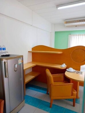 A compact hotel room with a kitchenette, a single bed, a small table with a chair, and a window with blinds. - Bella B Plus Hotel (Bangkok)