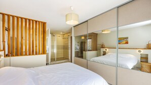 Habitación de hotel moderna con una cama grande, cabina de ducha de vidrio y un espejo amplio que refleja la habitación.