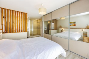 Ein modernes Hotelzimmer mit einem großen Bett, einer Duschkabine aus Glas und einem großen Spiegel, der den Raum reflektiert.