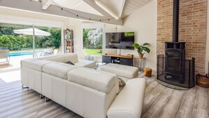Una sala de estar moderna con un sofá seccional, un televisor de pantalla plana, chimenea y vistas a una piscina y jardín.