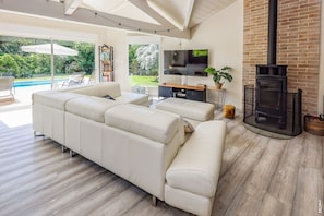 Ein modernes Wohnzimmer mit Ecksofa, Flachbildfernseher, Kamin und Blick auf Pool und Garten.